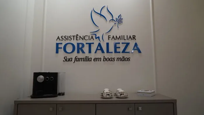 Recepção com a marca em relevo na parede — Assistência Familiar Fortaleza, Sua família em boas mãos — e um balcão com café